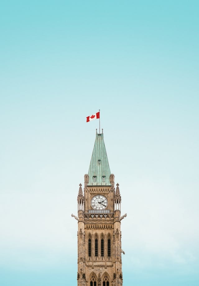 Canadian Parliament clock tower with flag under blue sky, representing Canada PR and immigration opportunities.