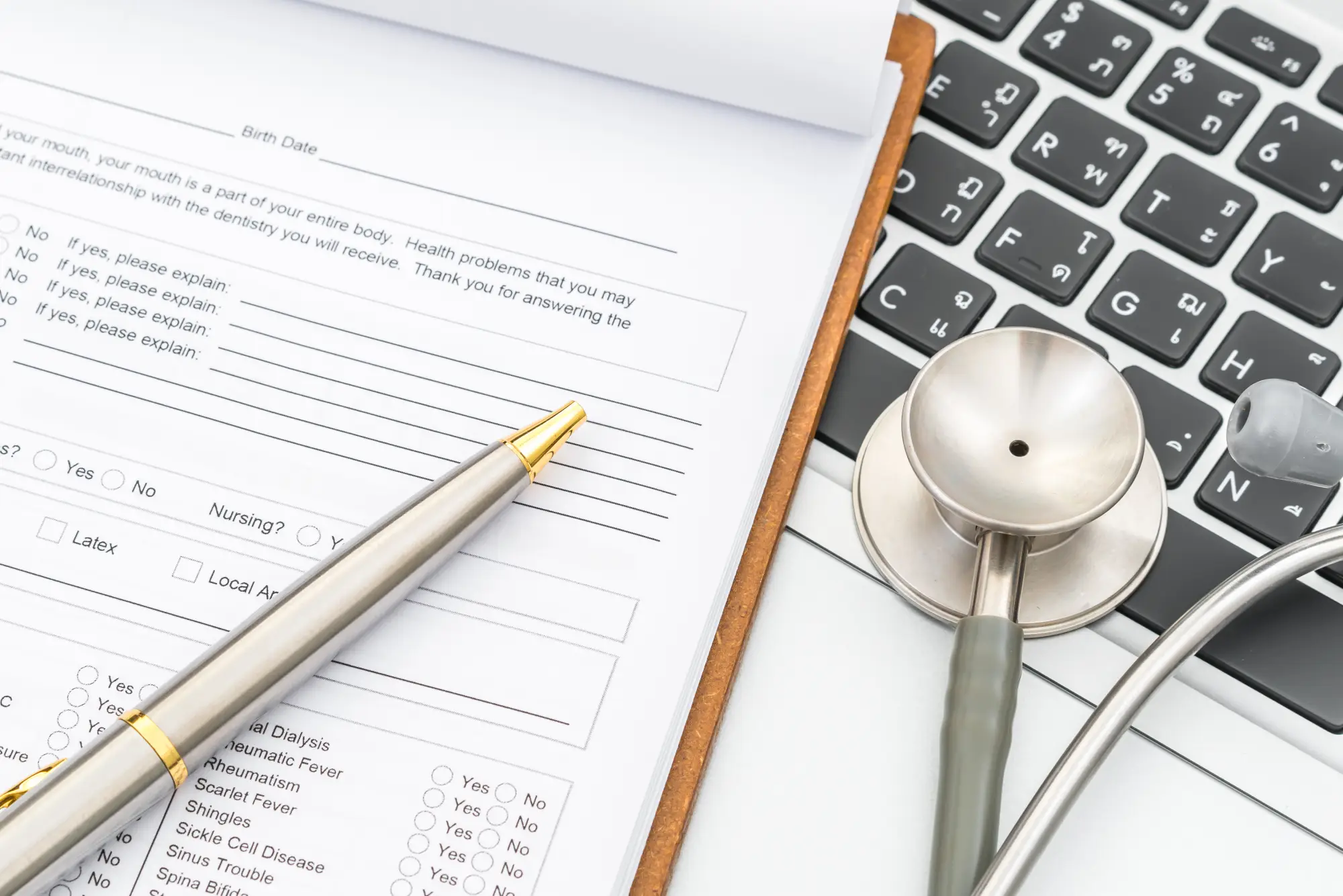 Close-up of a medical form with a pen and stethoscope placed on a laptop keyboard, representing the concept of medical inadmissibility.